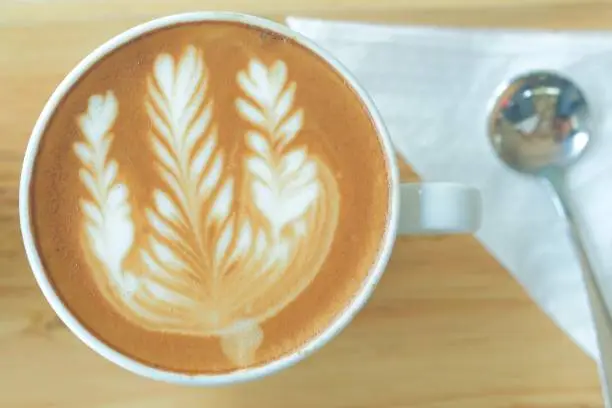 A cup of hot latte art with spoon and napkin in wooden tray