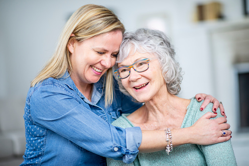 A woman and her grandmother are hugging and smiling while in their living room.
