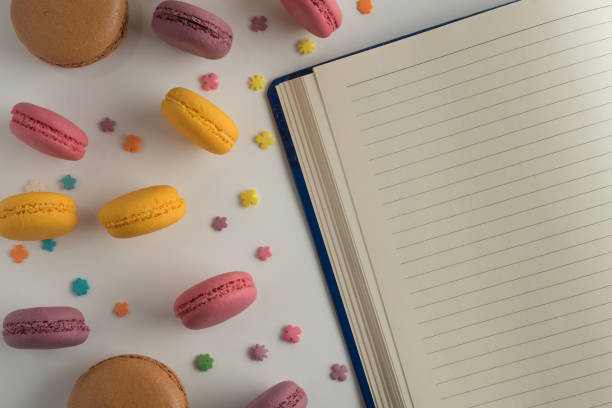 Biscuits macaron or macaroon on white background, colorful almond cookies with a diary to write a recipe, top view.