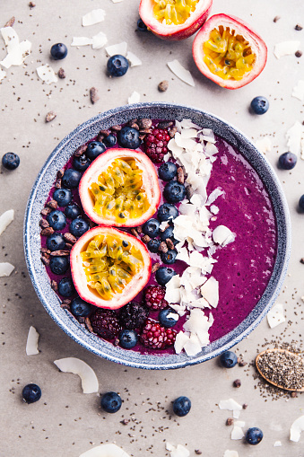 Tasty appetizing smoothie acai bowl made from blackberries and wild berries, decorated with cut passion fruit, coconut flakes, and cacao nibs. Served in bowl. Healthy life clean eating concept.