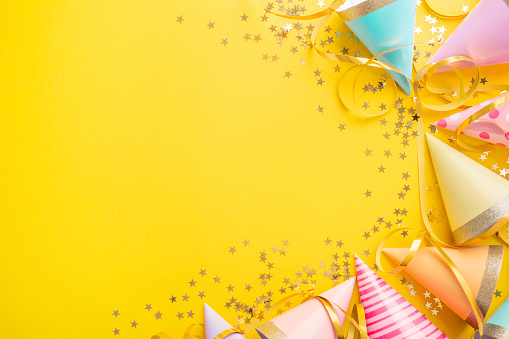 Colorful happy birthday or party background Flat Lay wtih birthday hats, confetti and ribbons on yellow background. Top View wit Copy space.