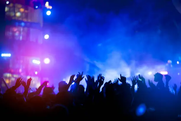 Photo of silhouettes of hand in concert.Light from the stage.confetti.the crowd of people silhouettes with their hands up.ribbon