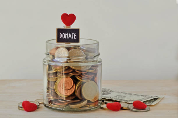 Money jar full of coins with Donate label and hearts - Charity concept stock photo