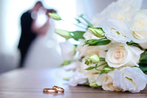 Photo of Wedding rings and bouquet on a background of blurred newlyweds