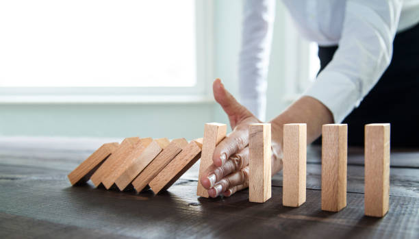 Stop the domino effect Businesswoman stopping falling wooden dominoes effect hand stopping dominos stock pictures, royalty-free photos & images
