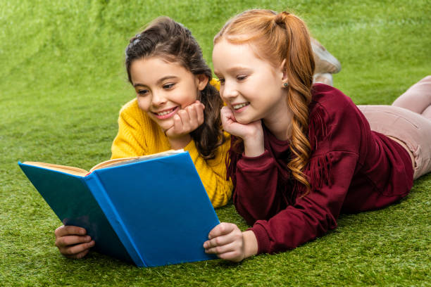 istock smiling schoolgirls lying on lawn and reading book 1089417838