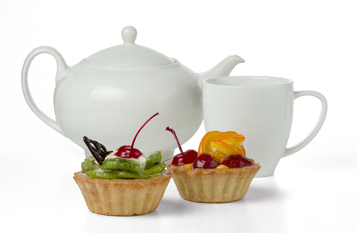 Colorful fruitcakes made with kiwi, orange, candied cherry, cream and chocolate isolated on a white background with a cup and a teapot.