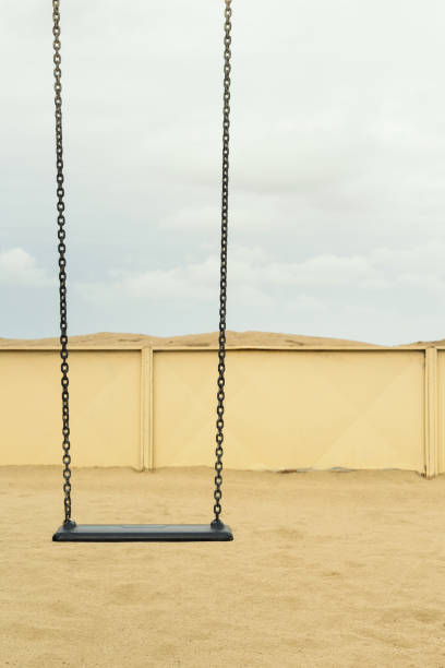 Empty swing at the winter beach, sand and cloudy sky