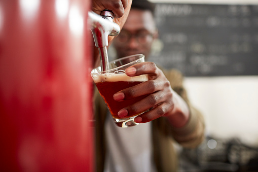 Young African bartender pouring beer in craft brewery.