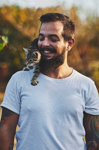Tattooed man on farm carrying cute kitten on his shoulder.