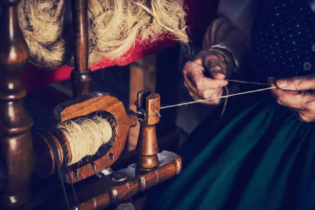 The old woman spinning wool using a traditional spinning wheel. She is wearing a traditional costume.