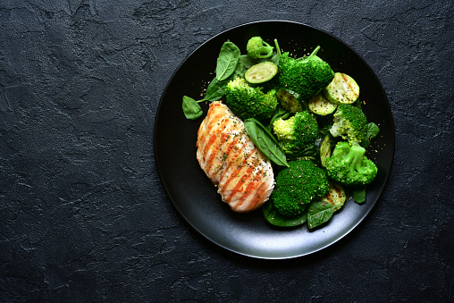Grilled chicken fillet with green vegetable salad on a black slate, stone or concrete background.Top view with copy space.