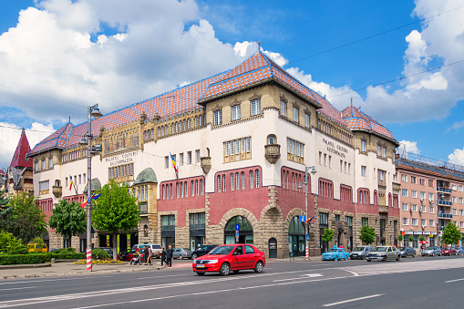 Cars and pedestrians move past the landmark, Art Nouveau style, Palace of Culture in downtown Targu Mures Romania on a sunny day.