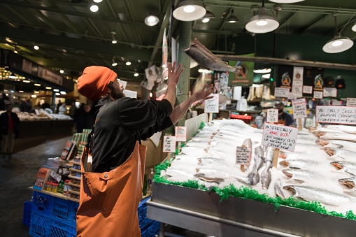 Seattle, USA - Dec 16, 2018: A fish Monger at Pike Place Market catching a fish for tourists late in the day.