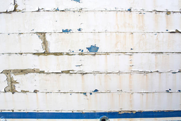 Abandoned and dilapidated boat hull background. Grungy Background image of an old boat hull that is rotting and weathered. The paint is peeling and scratched off. There are rust stains from the nails, the white peeling paint reveals blue flecks underneath, and under that you can see the exposed wood planks of the old vessel. You can also see nail holes and at the bottom is a blue painted keel line. A great abstract grunge or industrial background wallpaper that you can use for a grunge illustration technique