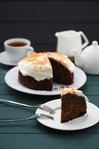 Chocolate fruit cake with cream cheese glasing and orange peel served with black tea on dark background copyspace