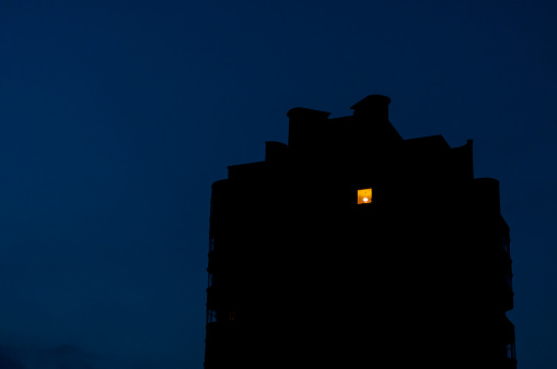 Night view on old residential building where the light in on only in one room on the highest floor