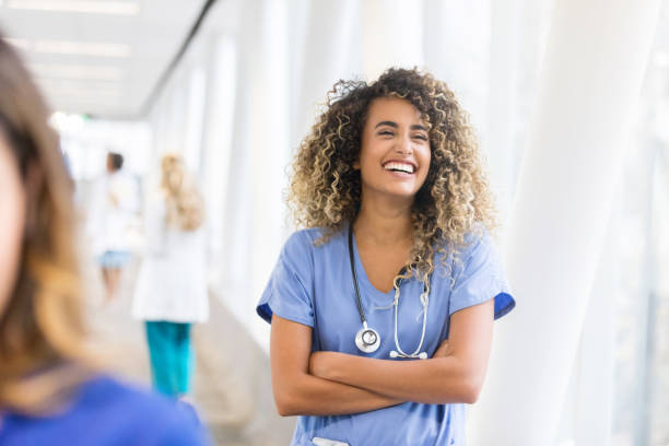 Cheerful nurse in hospital skybridge Confident young female healthcare professional laughs while standing in a hospital skybridge. medical occupation stock pictures, royalty-free photos & images
