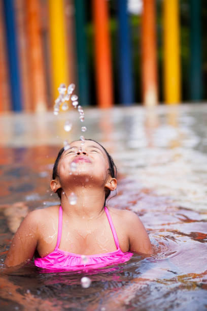 Latin girl between 5 to 7 years old plays alone in the pool making water for the sky and enjoying while smiling and having a lot of fun in a very nice day