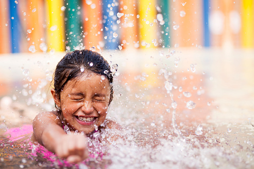 Latin girl between 5 to 7 years old plays alone in the pool making water for the sky and enjoying while smiling and having a lot of fun in a very nice day
