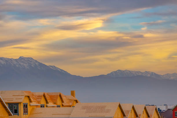 New construction homes in front of Utah Valley mountains and sunset. Rooftops of the homes shown all in a line. Development is really picking up in Utah Valley.