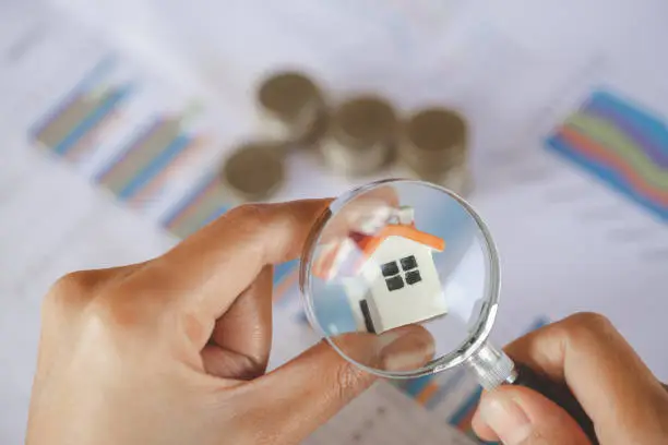 Photo of Close-up Of A Businessperson's Hand Looking At House Model Through Magnifying Glass, House searching concept with a magnifying glass