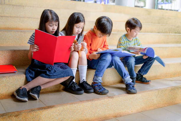 niedliche kleine asiatische kinder lesebücher zusammen sitzend auf schritte im freien - reading and writing little boys reading asian ethnicity stock-fotos und bilder