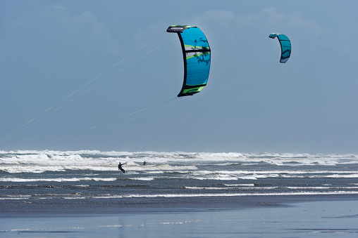 A couple of kite surfers amongst the waves near the shore on a windy day