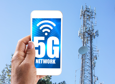 5G Cell Tower: 5G communications towern with woman holding mobile phone