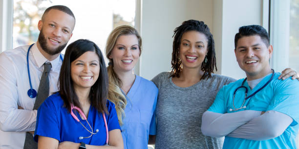 Diverse healthcare team of doctors and nurses standing in hospital hallway Diverse group of nurses, doctors, and other healthcare professionals are standing together confidently in a hospital hallway. medical occupation stock pictures, royalty-free photos & images
