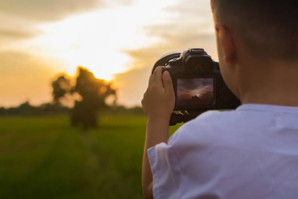 Cute asian boy learning to taking photo from DSLR Camera in his hand with nature outdoor background.
