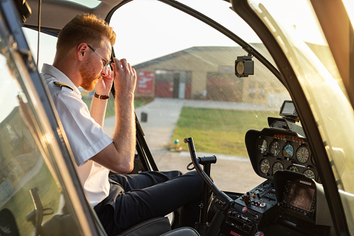 Helicopter pilot sitting in cockpit, taking off sunglasses and looking at control panel