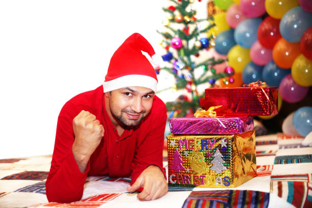 Young handsome man laying with Christmas presents and looking at camera.
