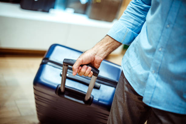 grande valigia da viaggio blu navy tenuta da una persona irriconoscibile in un negozio di borse e accessori - valigia a rotelle foto e immagini stock