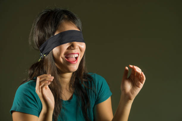 giovane ragazza adolescente asiatica coreana bendata felice e carina eccitata giocando pericolosa sfida virale su internet isolata su sfondo scuro sotto una luce di studio spigolosa e drammatica - blindfold foto e immagini stock