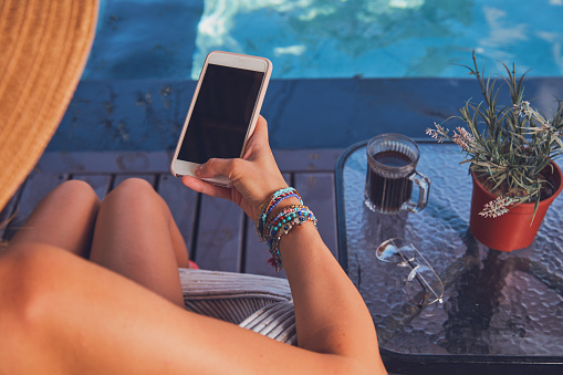 Girl using cellphone while lying on a swimming pool deck lounge bed.