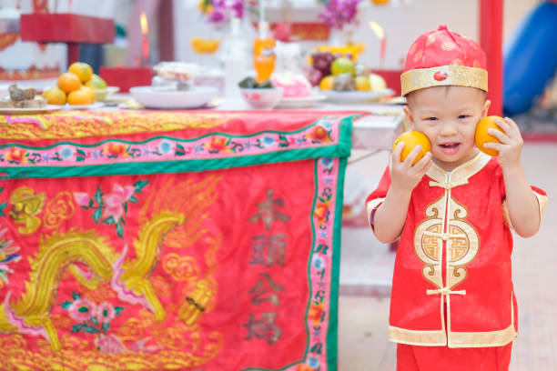 bonitos pouco 2 anos de idade da criança asiática bebê menino no chinês tradicional vermelho terno segurando laranja sagrada no templo chinês local - chinese ethnicity chinese culture china 2 3 years - fotografias e filmes do acervo