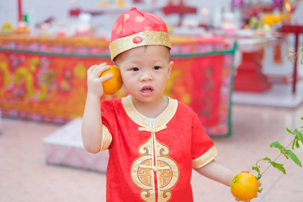bonitos pouco 2 anos de idade da criança asiática bebê menino no chinês tradicional vermelho terno segurando laranja sagrada no templo chinês local - chinese ethnicity chinese culture china 2 3 years - fotografias e filmes do acervo