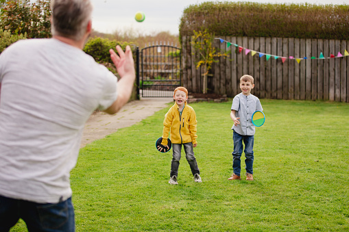 Rear view of a mid adult father throwing a tennis ball to his son and his friend. They are having fun and playing a game.