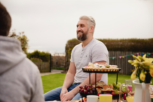 Over the shoulder view of a mid adult man laughing and smiling while at a easter garden party.