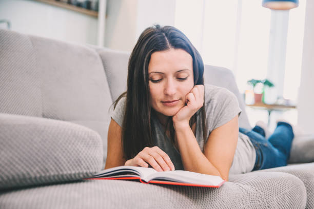 istock A woman reads a book lying on the couch 1089668908