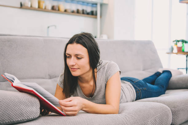 istock A woman reads a book lying on the couch 1089668912