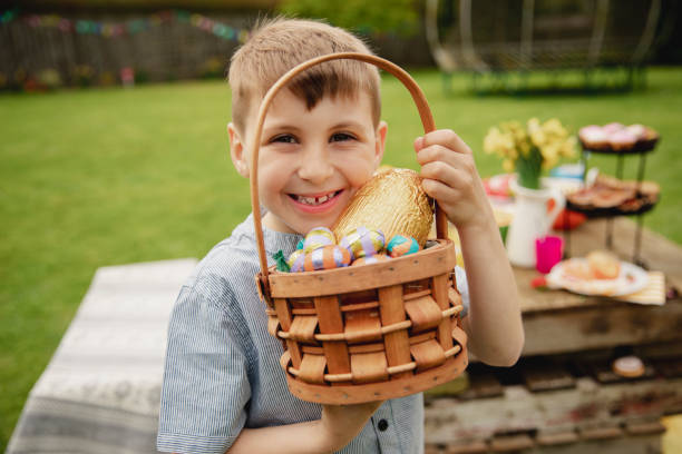 He Loves Chocolate Eggs Young boy standing outdoors holding a basket full of chocolate easter eggs that he found on the easter egg hunt. holding child flower april stock pictures, royalty-free photos & images