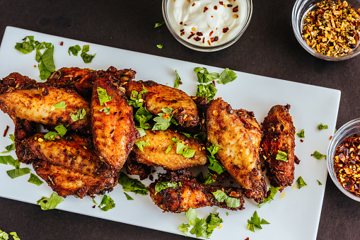 Spicy Chicken Wings with Cilantro, White Sauce and Chili Flakes on White Platter, Dark Background Photo