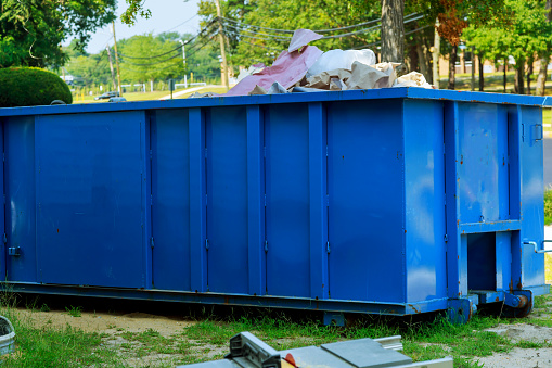 Blue metal waste container with building debris, industrial garbage bin