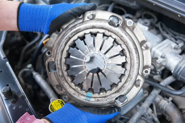 Mechanic wearing protective work gloves holds old clutch pressure plate over a car engine