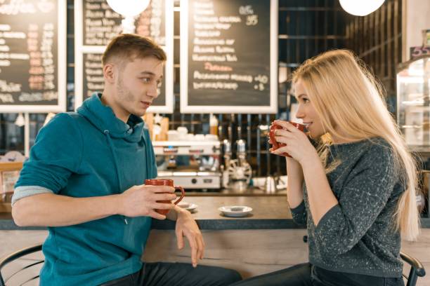 若い男性と女性のバーのカウンター、カップル喫茶、友達の近くに座ってコーヒー ショップで話して一緒に笑みを浮かべてコーヒー - drinking couple bar counter bar ストックフォトと画像