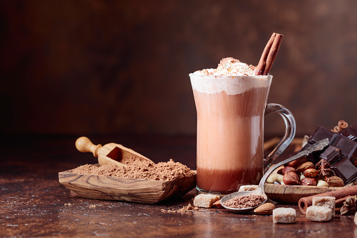 Cocoa with cream, cinnamon, chocolate pieces and various spices on a brown background. Copy space for your text.