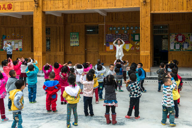 Zhao Xing, China - April 22, 2015: Guizhou province, Zhaoxing, China - Chinese preschool children are exercising and dancing in a row  led by teachers and trainees.\nSHOT FROM THE PUBLIC ROAD !!