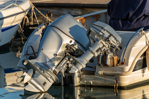 Detail of two outboard motors (engines), on a boat moored in the port with reflections